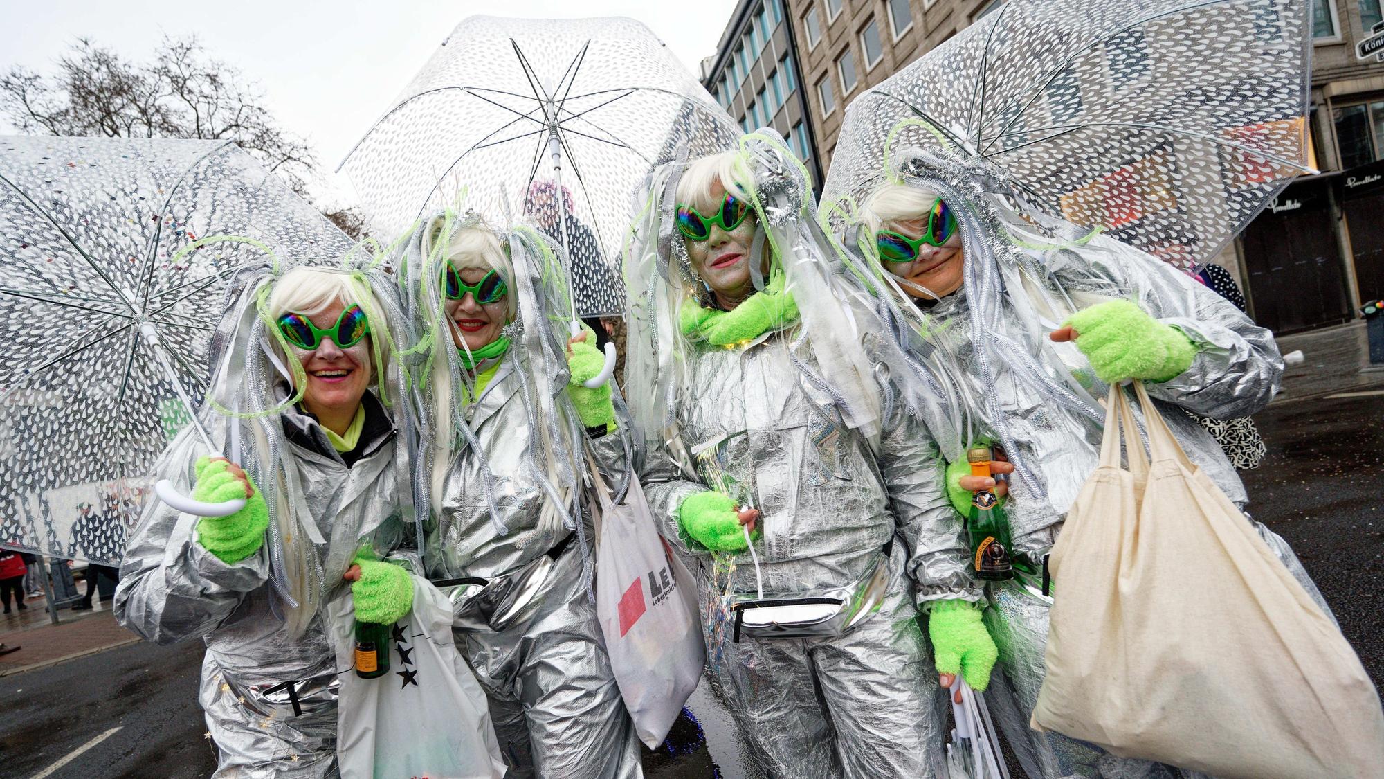 Jecken halten beim traditionellen Kö-Treiben auf der Düsseldorfer Königsallee Schirme gegen den Regen.