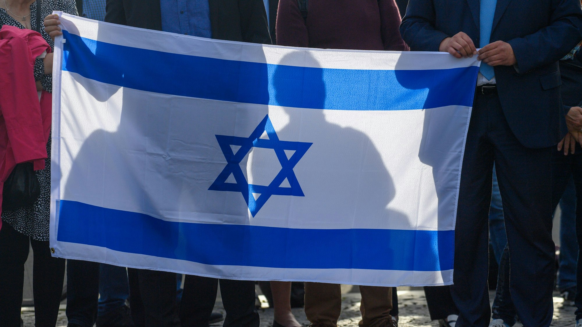 Teilnehmer einer Solidaritätskundgebung für Israel halten die Fahne Israels in den Händen. Terroristen hatten am Samstag im Auftrag der im Gazastreifen herrschenden Hamas ein Massaker unter israelischen Zivilisten in Grenzorten und auf einem Musikfestival angerichtet. +++ dpa-Bildfunk +++