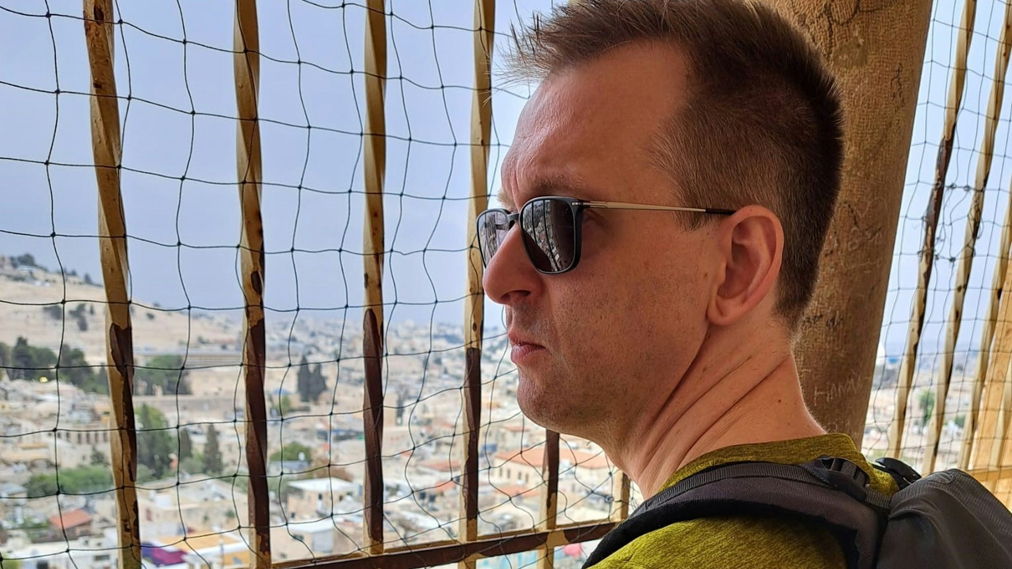Pastor Oliver Dannenberg steht an der Erlöserkirche in Jerusalem und blickt durch ein Gitter auf die Stadt.