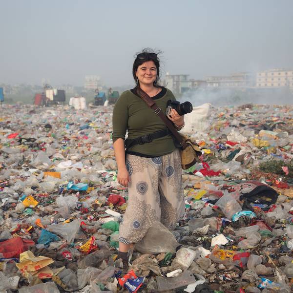 Alena Horst steht mit Kamera in der Hand in einer Müll-Landschaft.