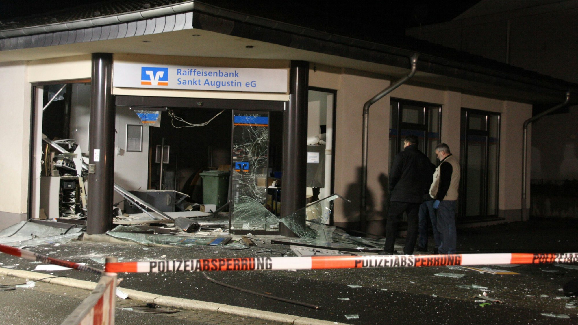 Zwei Personen schauen sich am Tatort einer Geldautomatensprengung in einer Raiffeisenbank in Sankt Augustin um. (Archivbild)
