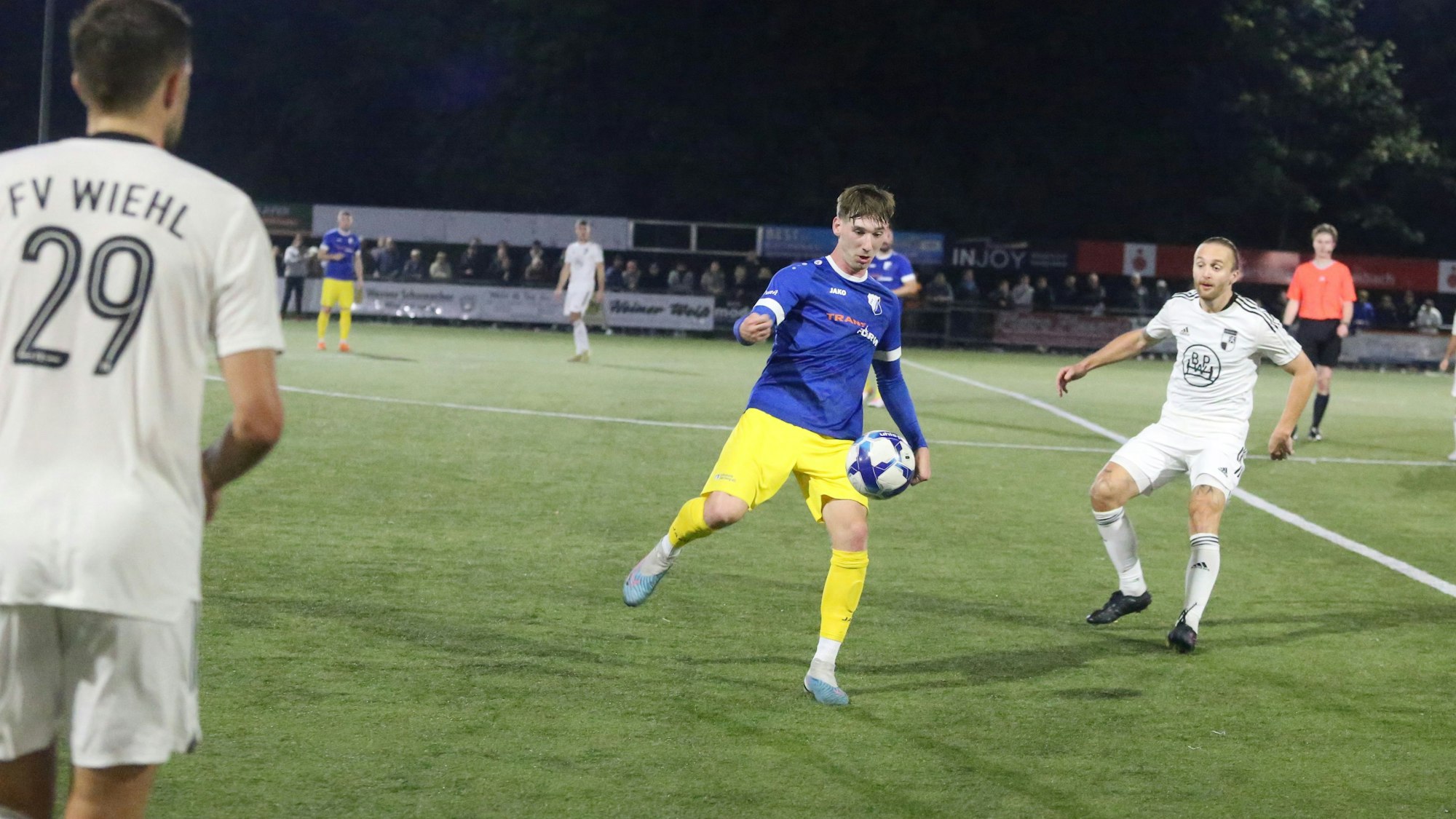 Flankiert von zwei Wiehler Fußballern schießt ein Nümbrechter den Ball nach vorne.