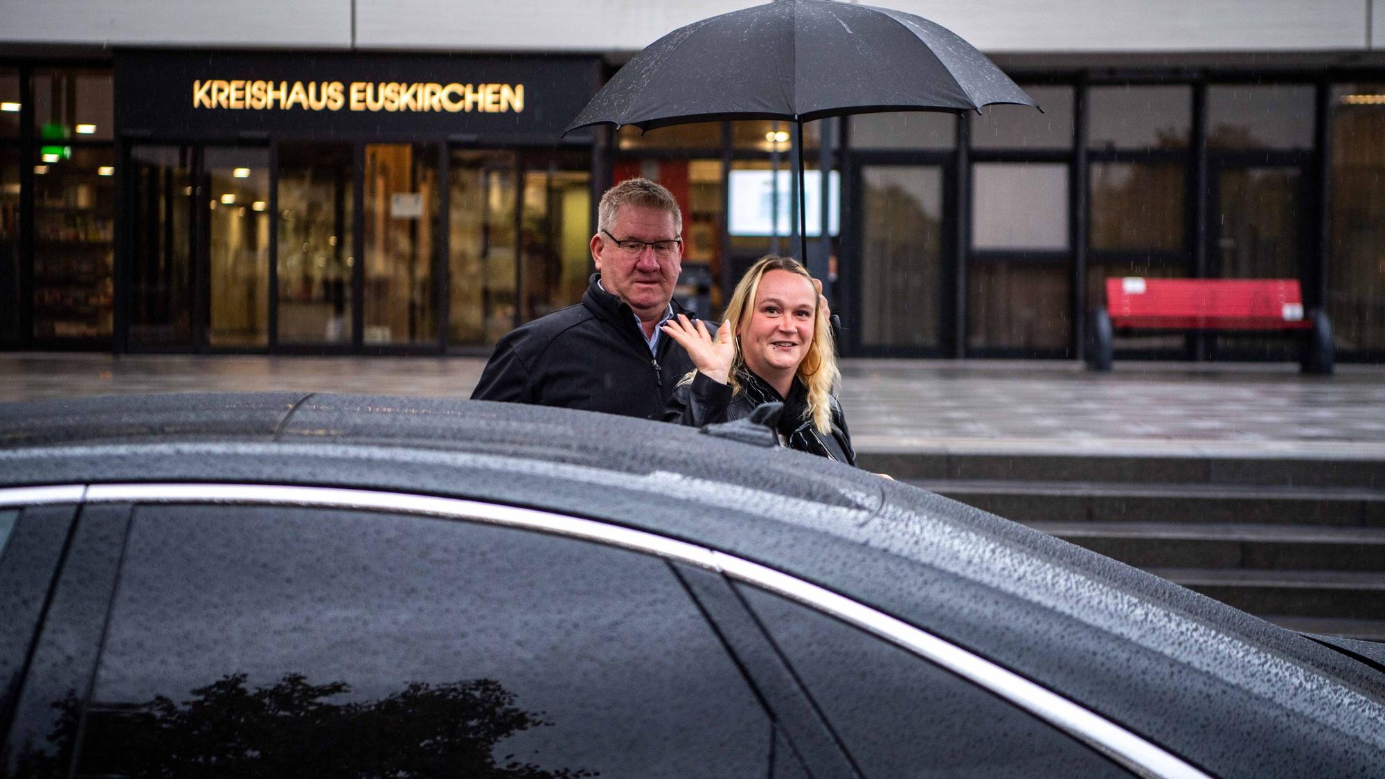 Das Bild zeigt Werner Krebs, wie er vor dem Kreishaus Simone Limbach den Schirm hält. Sie winkt in die Kamera.