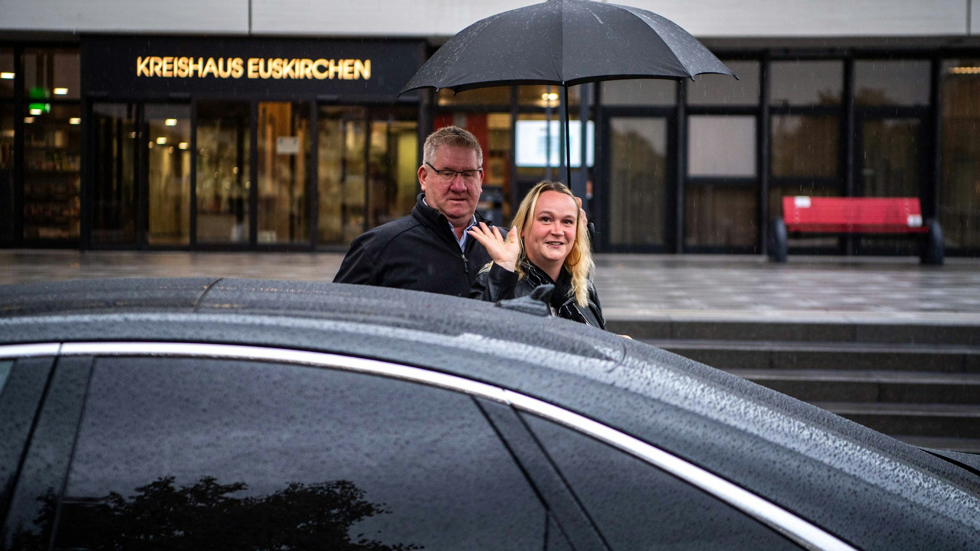 Das Bild zeigt Werner Krebs, wie er vor dem Kreishaus Simone Limbach den Schirm hält. Sie winkt in die Kamera.