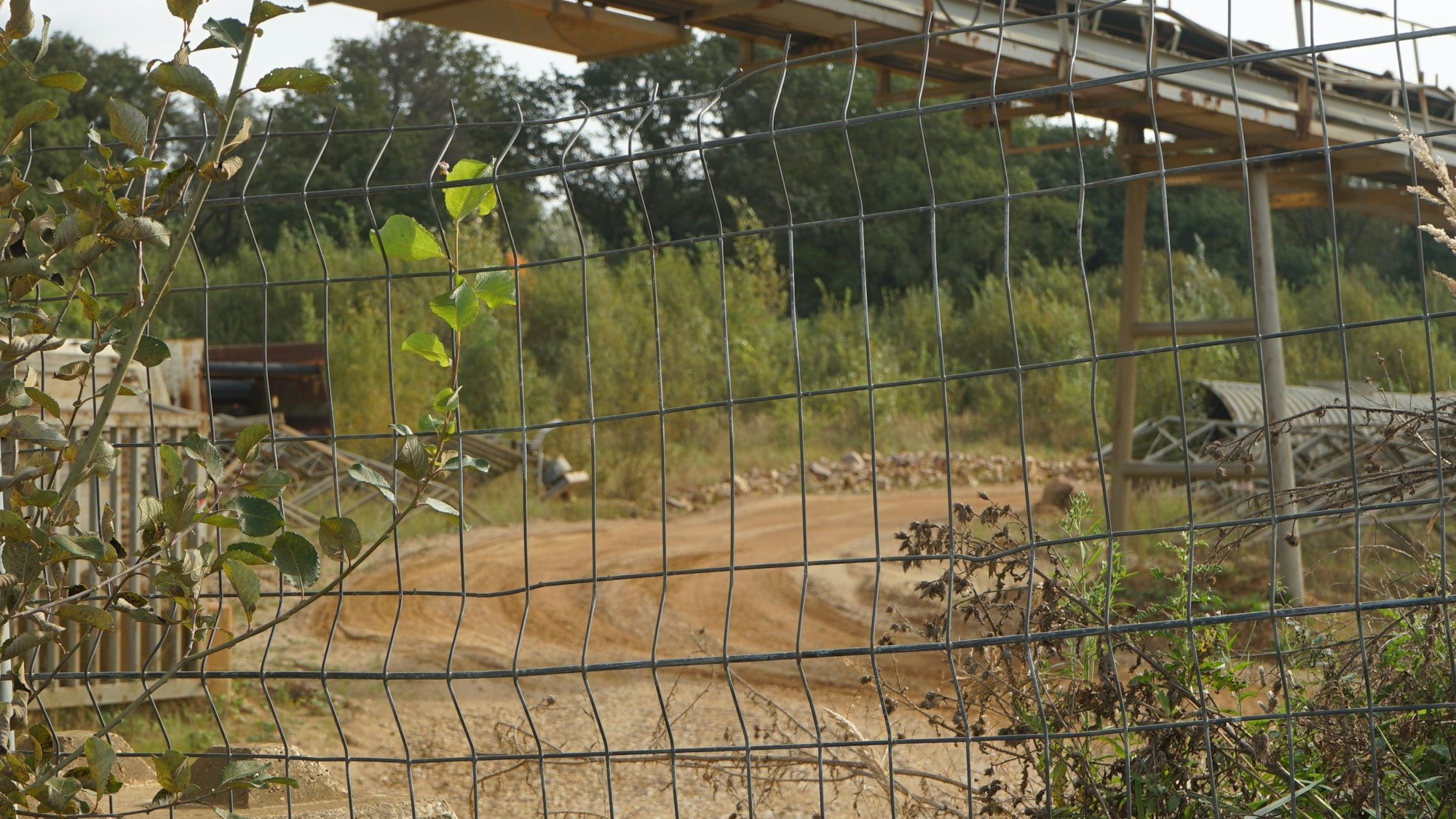 Ein Förderband einer Kiesgrube, davor steht ein Bauzaun.