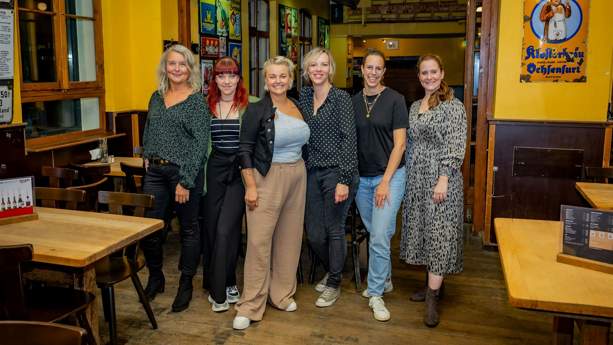Mica Frangenberg (v.l.), Jo Eicker, Nici Kempermann, Sophie Gesthuysen, Anna Heller, Nadine Krahforst und Vera Drewke (nicht auf dem Bild) stehen in einer Kneipe.