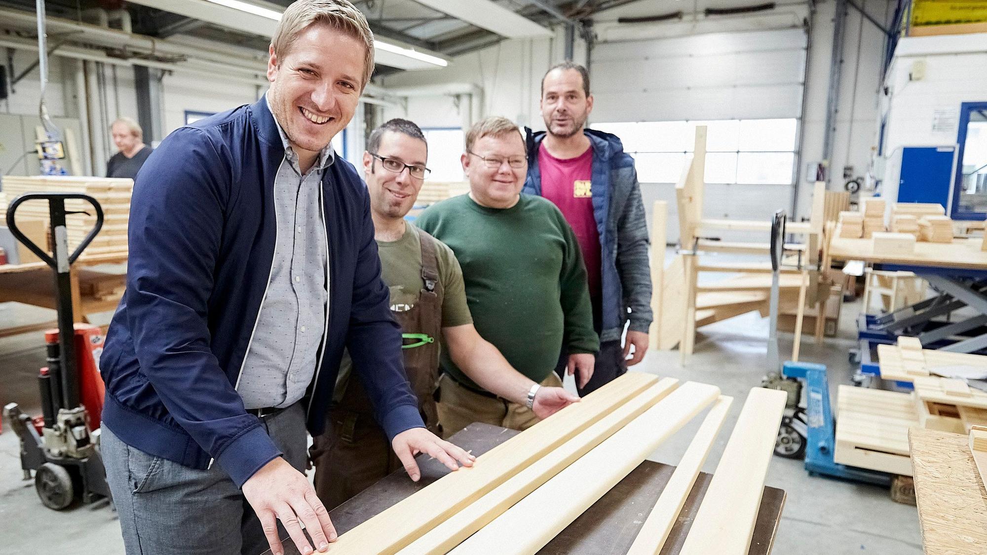 Das Bild zeigt Landrat Markus Ramers, wie er mit NEW-Mitarbeitern in der Schreinerwerkstatt steht. Vor ihnen liegt Holz.