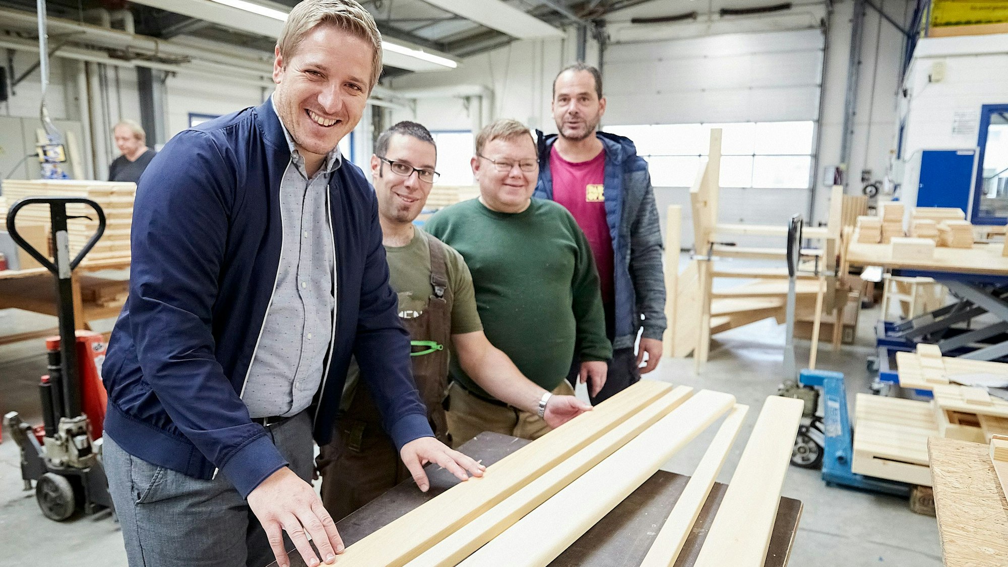Das Bild zeigt Landrat Markus Ramers, wie er mit NEW-Mitarbeitern in der Schreinerwerkstatt steht. Vor ihnen liegt Holz.