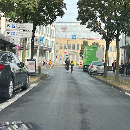 Zwei Radfahrer sind auf der unteren Hauptstraße in Richtung Schrankenkreisel und Rhein-Berg-Galerie unterwegs.