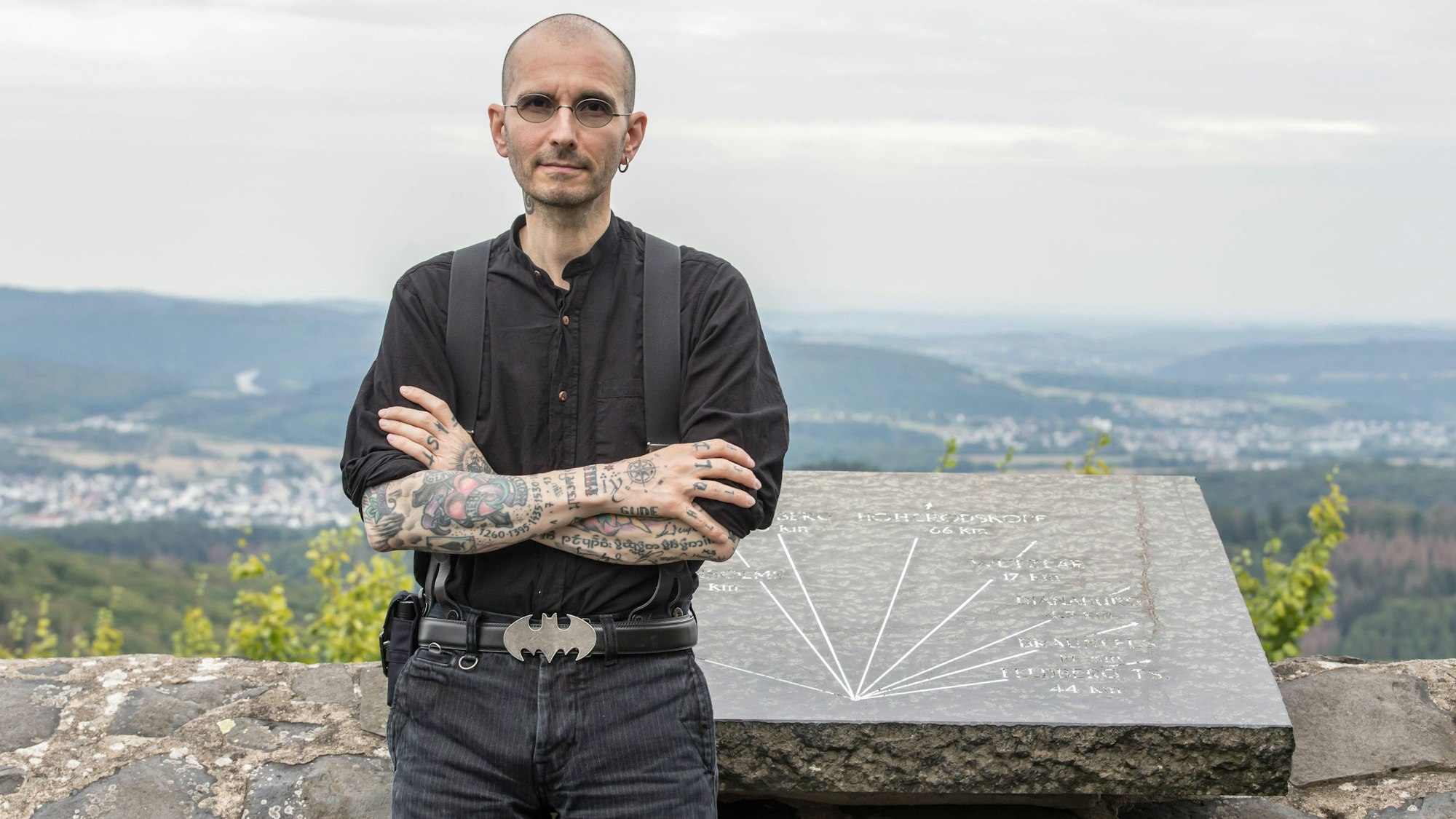 Der bekannte Kölner Kriminalbiologe Mark Benecke steht an einer Mauer, hinter ihm ist eine weite Landschaft und ein Tal zu sehen.