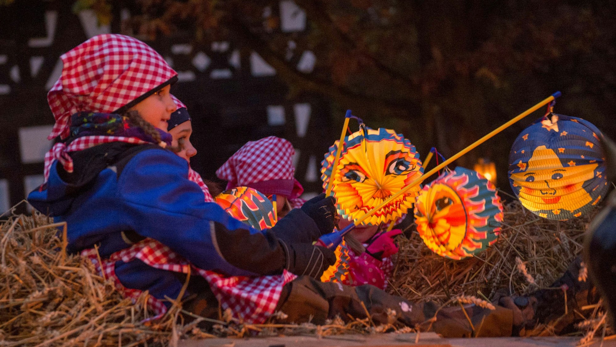 Kinder sitzen auf einem Wagen, der mit Stroh ausgelegt ist und halten Laternen in den Händen.
