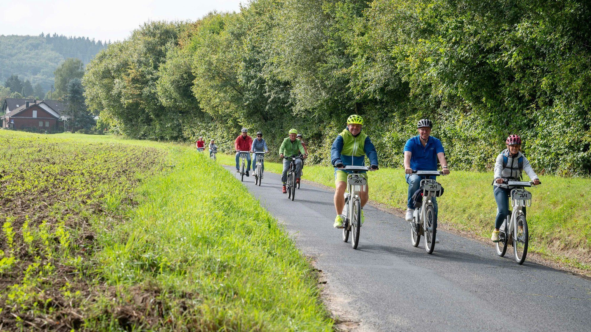 Eine Gruppe radelt auf einem asphaltierten Weg zwischen Feld und Wald.