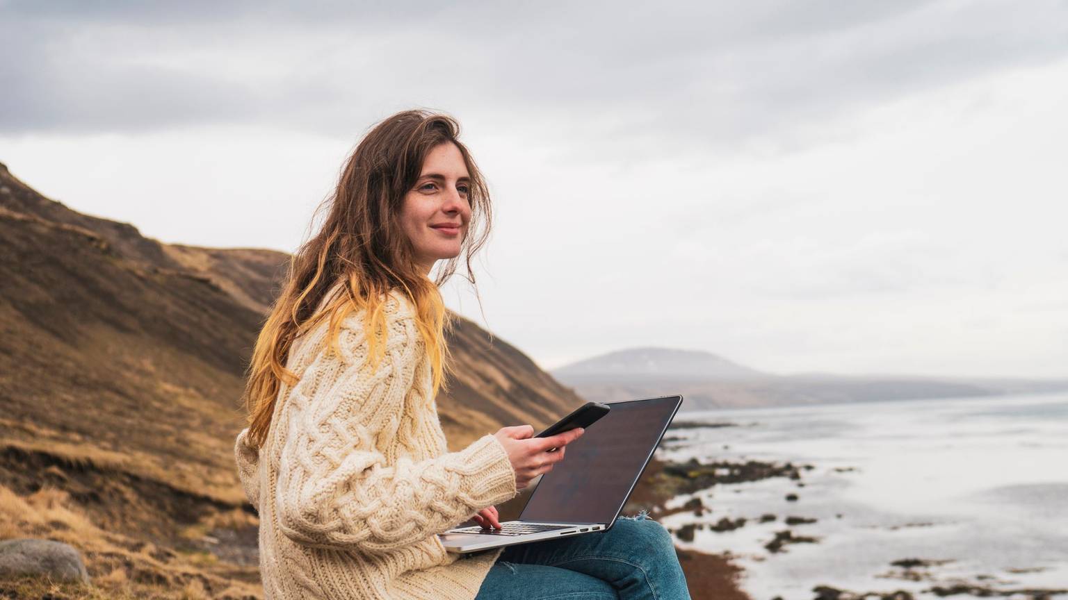 Frau sitzt mit Laptop am Meer