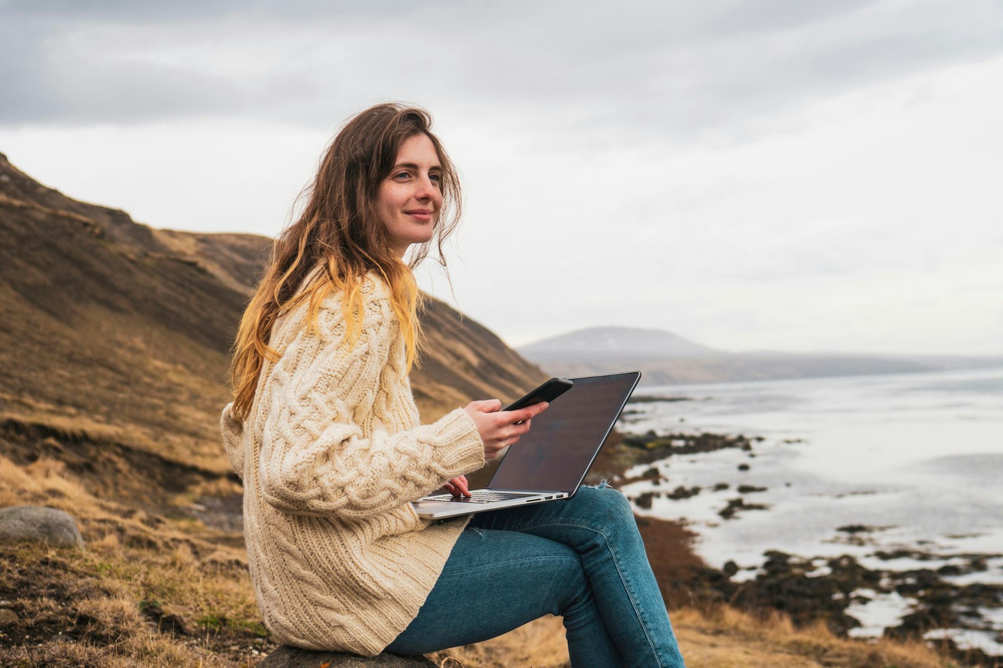 Frau sitzt mit Laptop am Meer