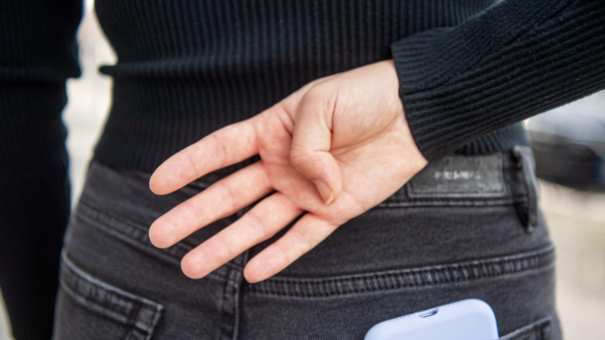 Eine Frau hält ihre Hand hinter den Rücken, die Innenseite gezeigt und nur den Daumen angewinkelt.