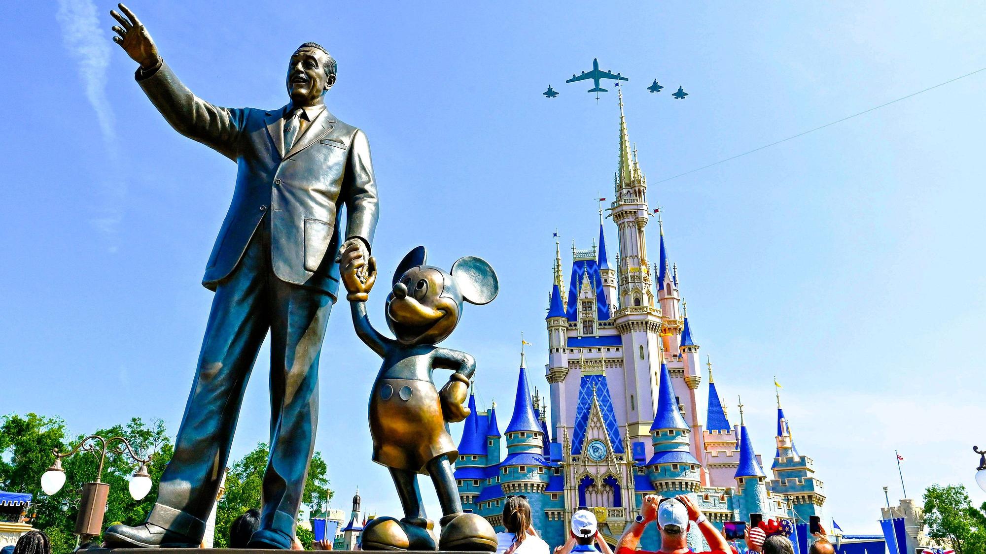 Die Staturen von Walt Disney und Mickey Mouse in der Disney World. Im Hintergrund überfliegen Flugzeuge das Cinderella Schloss.