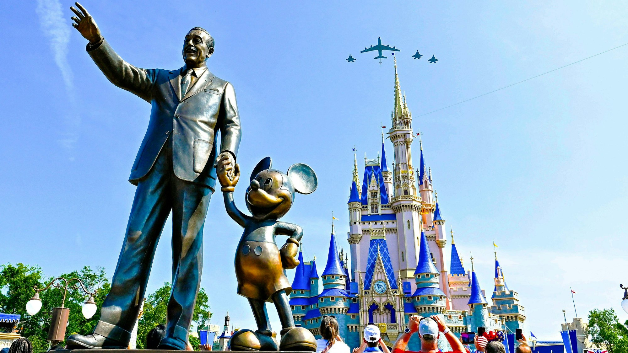 Die Staturen von Walt Disney und Mickey Mouse in der Disney World. Im Hintergrund überfliegen Flugzeuge das Cinderella Schloss.
