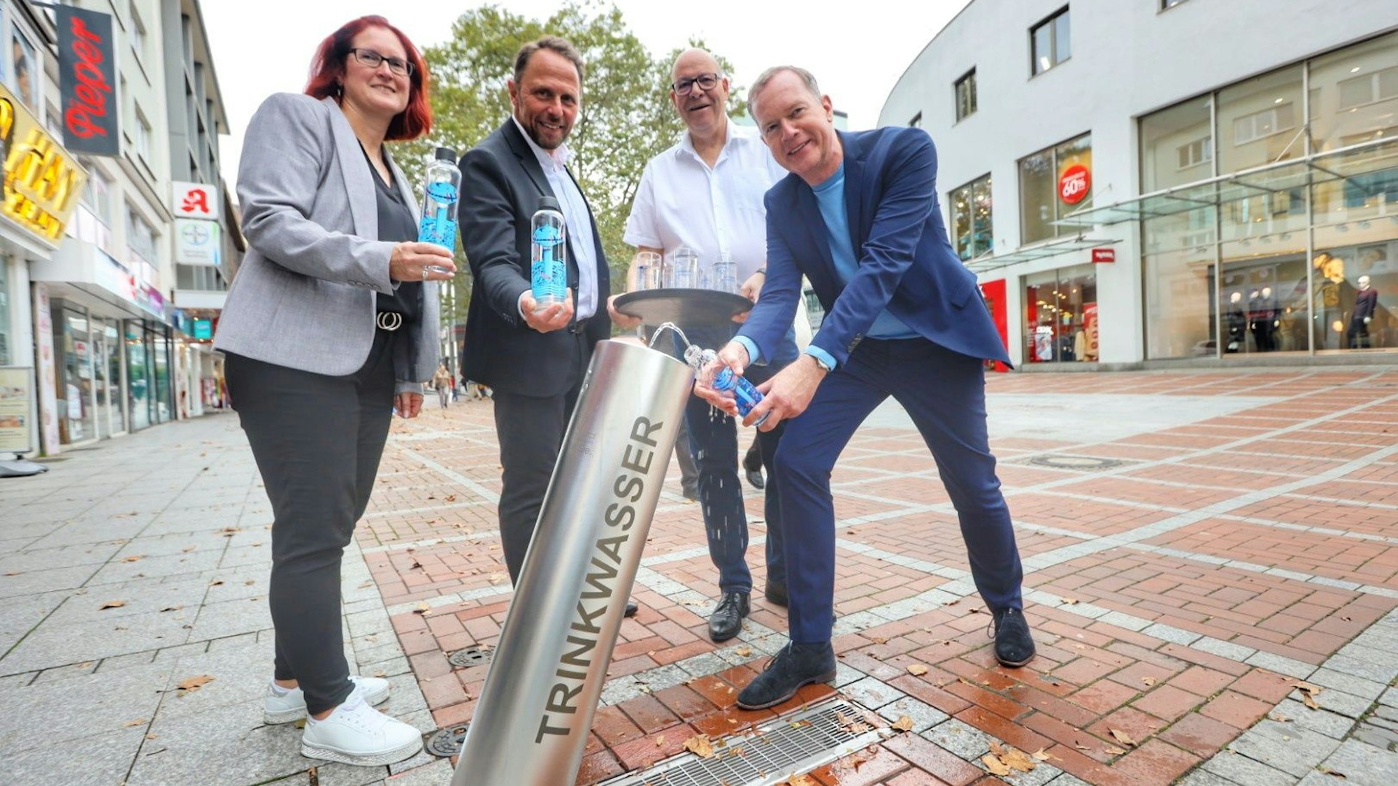 Drei Männer und eine Frau stehen am Trinkwasserbrunnen in Wiesdorf.