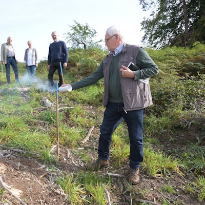 Josef Koll besprüht einen Holzstecken im Wald mit blauer Farbe.