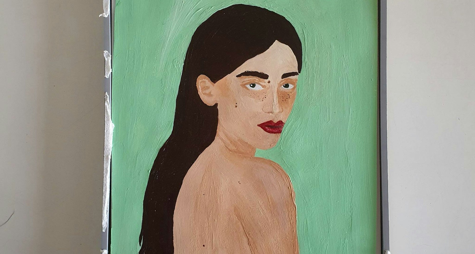 Das Bild zeigt eine Frau mit langen dunklen Haaren und nacktem Oberkörper auf grünem Grund. Sie schaut über die Schulter in Richtung der Betrachtenden.