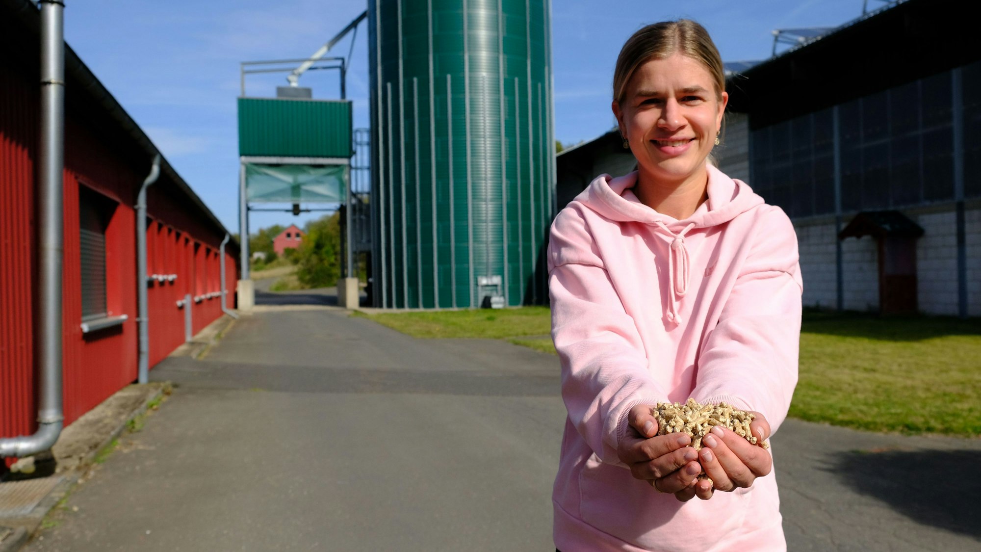 Catharina Hartges hält mit beiden Händen Holzpellets in die Kamera. Im Hintergrund ist ein Siloturm zu erkennen.