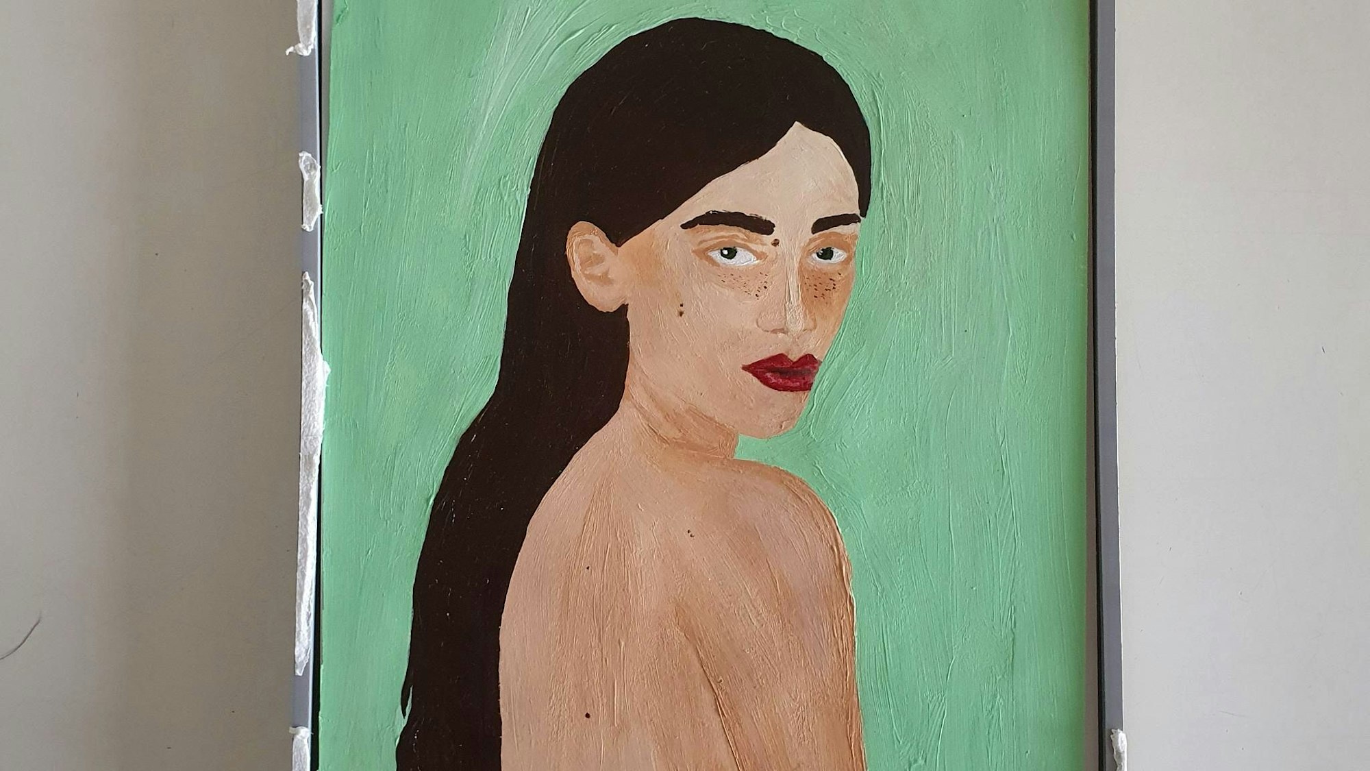 Ein Gemälde ist zu sehen. Es zeigt eine junge, unbekleidete, schwarzhaarige Frau, die über ihre Schulter blickt. Der Hintergrund des Gemäldes ist türkisfarben.