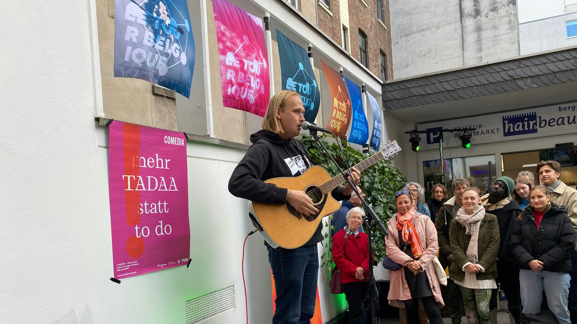 Ein Mann spielt auf einem Straßenfestival vor Publikum Gitarre und singt in ein Mikrofon.