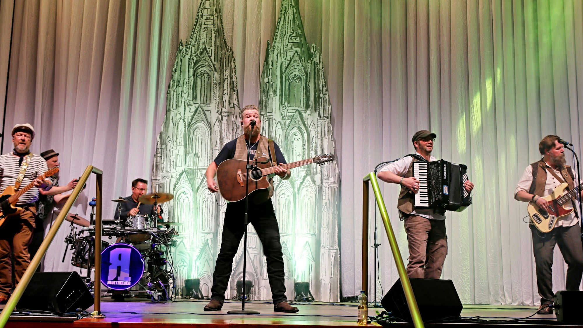 Die Band steht auf der Bühne, im Bühnenbild ist der Dom zu sehen.