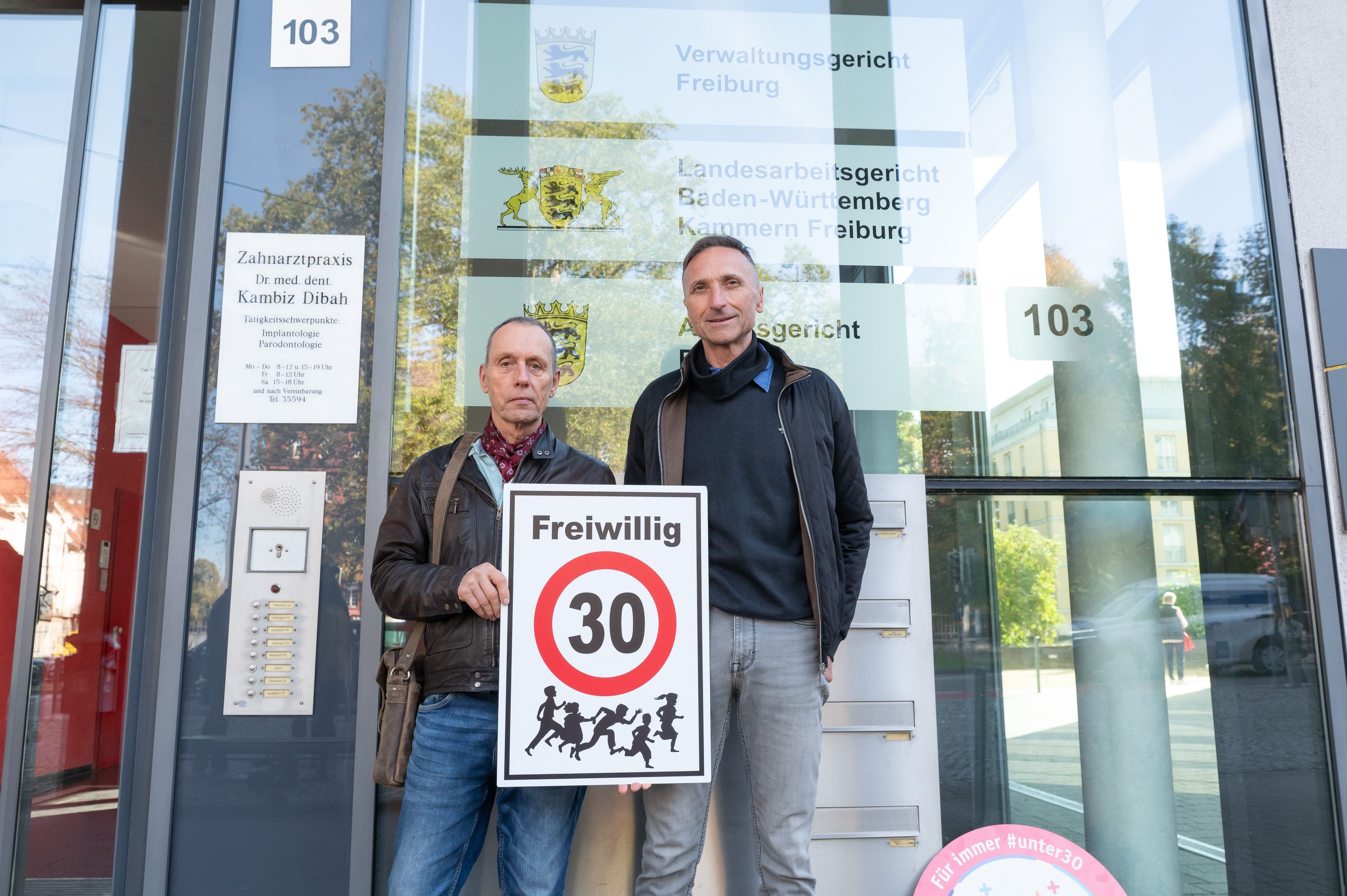 Christian Kronbitter (l) und Erich Maier halten vor dem Verwaltungsgericht ein Schild mit der Aufschrift „Freiwillig 30“ in die Kamera. Das Verwaltungsgericht Freiburg verhandelt über mehrere von der Deutschen Umwelthilfe (DUH) unterstützte Klagen zur Klärung der Frage, ob die Aufstellung von ·Freiwillig Tempo 30-Schildern rechtmäßig ist.