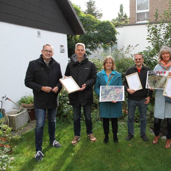 Drei Männer und drei Frauen stehen mit Fotos und Siegerurkunden in einem gepflegten Siegburger Garten