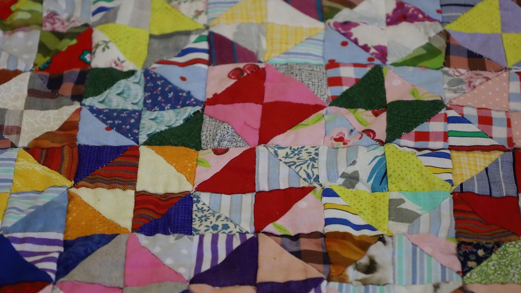 Das Bild zeigt einen Ausschnitt einer Patchwork-Decke, die aus Hunderten von kleinen, aneinander genähten Stoffstücken besteht.