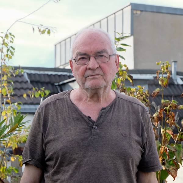 Ein älterer Mann mit Brille steht vor Pflanzen auf einer Terrasse.