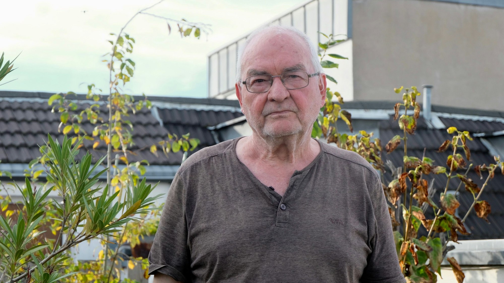 Ein älterer Mann mit Brille steht vor Pflanzen auf einer Terrasse.