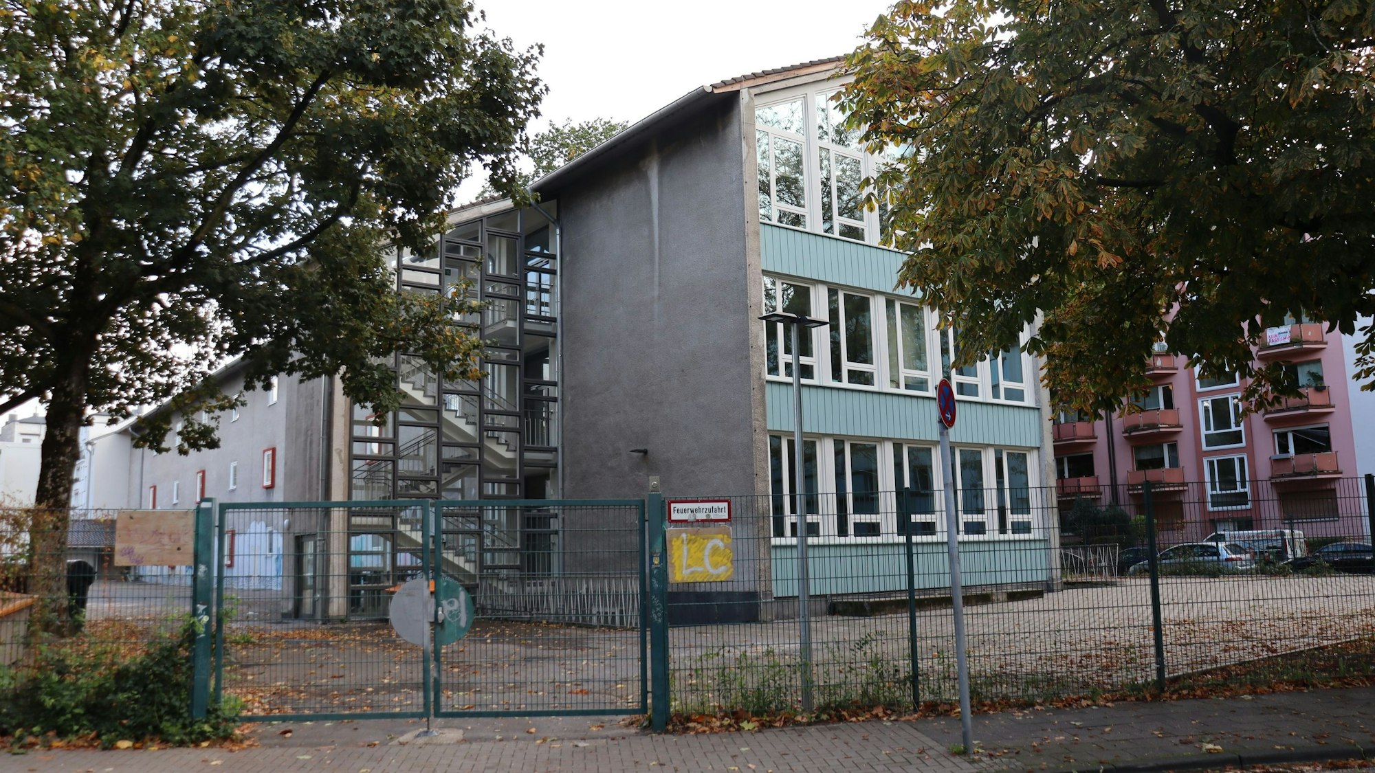 Hinter einem Zaun ist ein blau-graues Schulgebäude zu sehen.