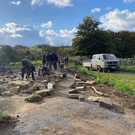 Menschen behauen große Grauwackesteine für eine Trockenmauer.