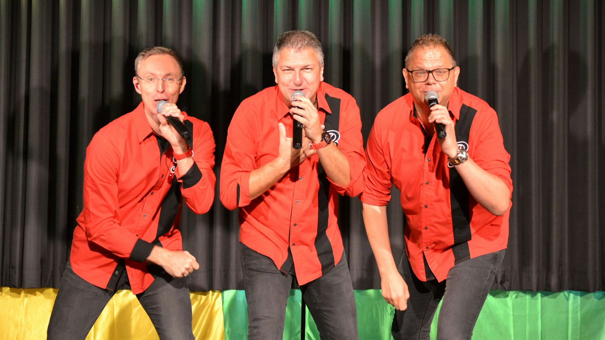 Die drei Sänger der Band „Bremsklötz“ tragen identische rote Hemden und singen in Mikrofone.