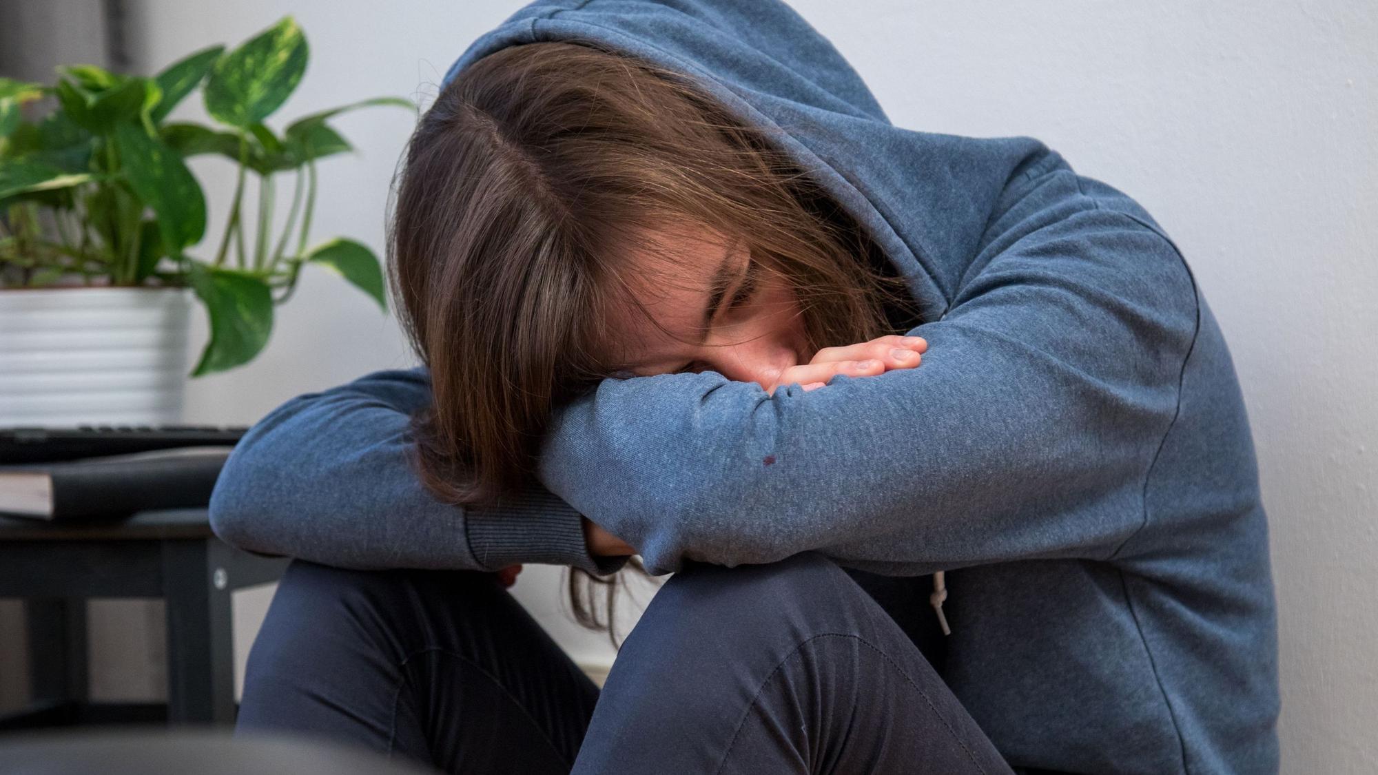 Ein Junge im blauen Kapuzenpulli lässt den Kopf hängen.