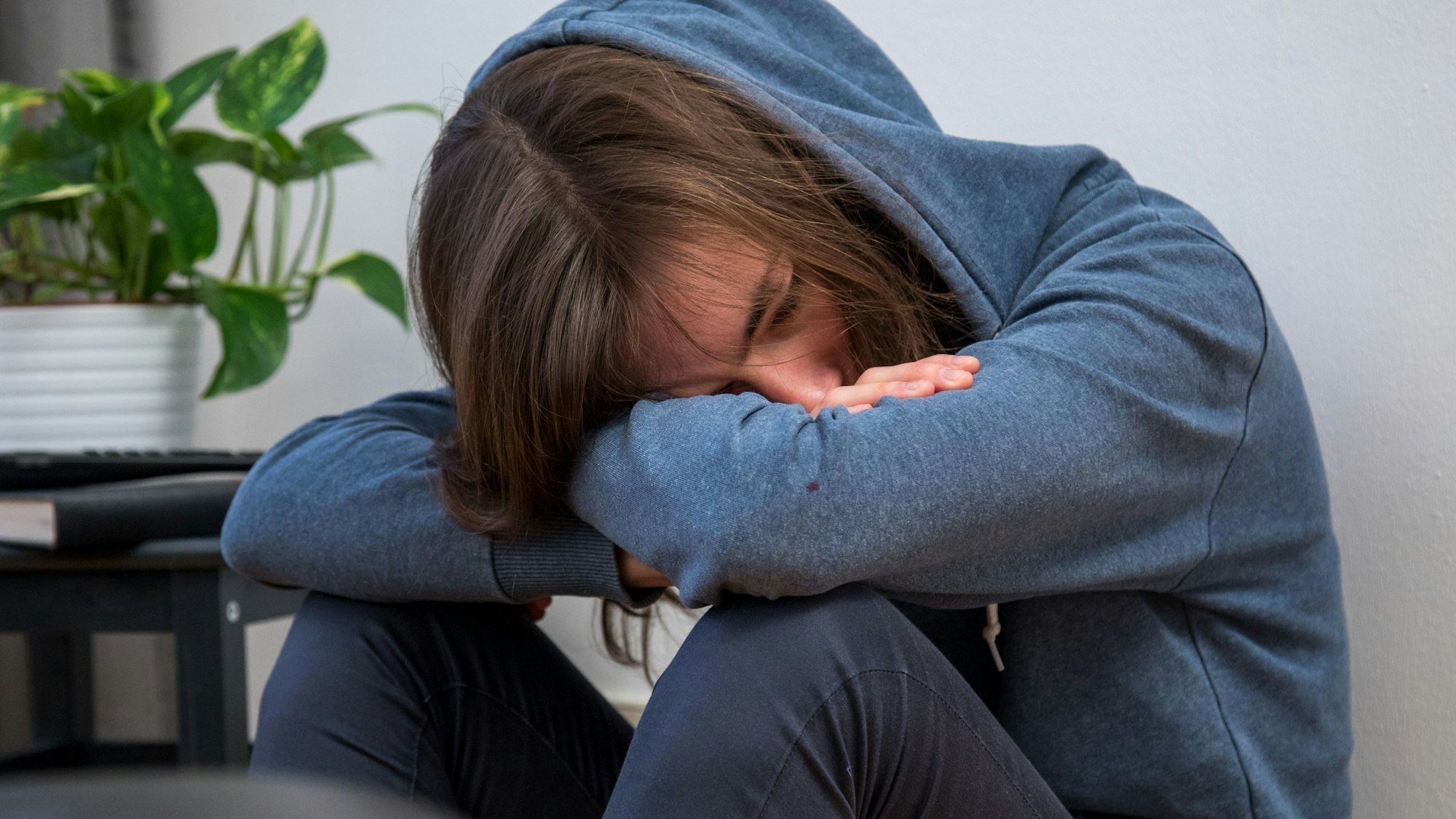Ein Junge im blauen Kapuzenpulli lässt den Kopf hängen.