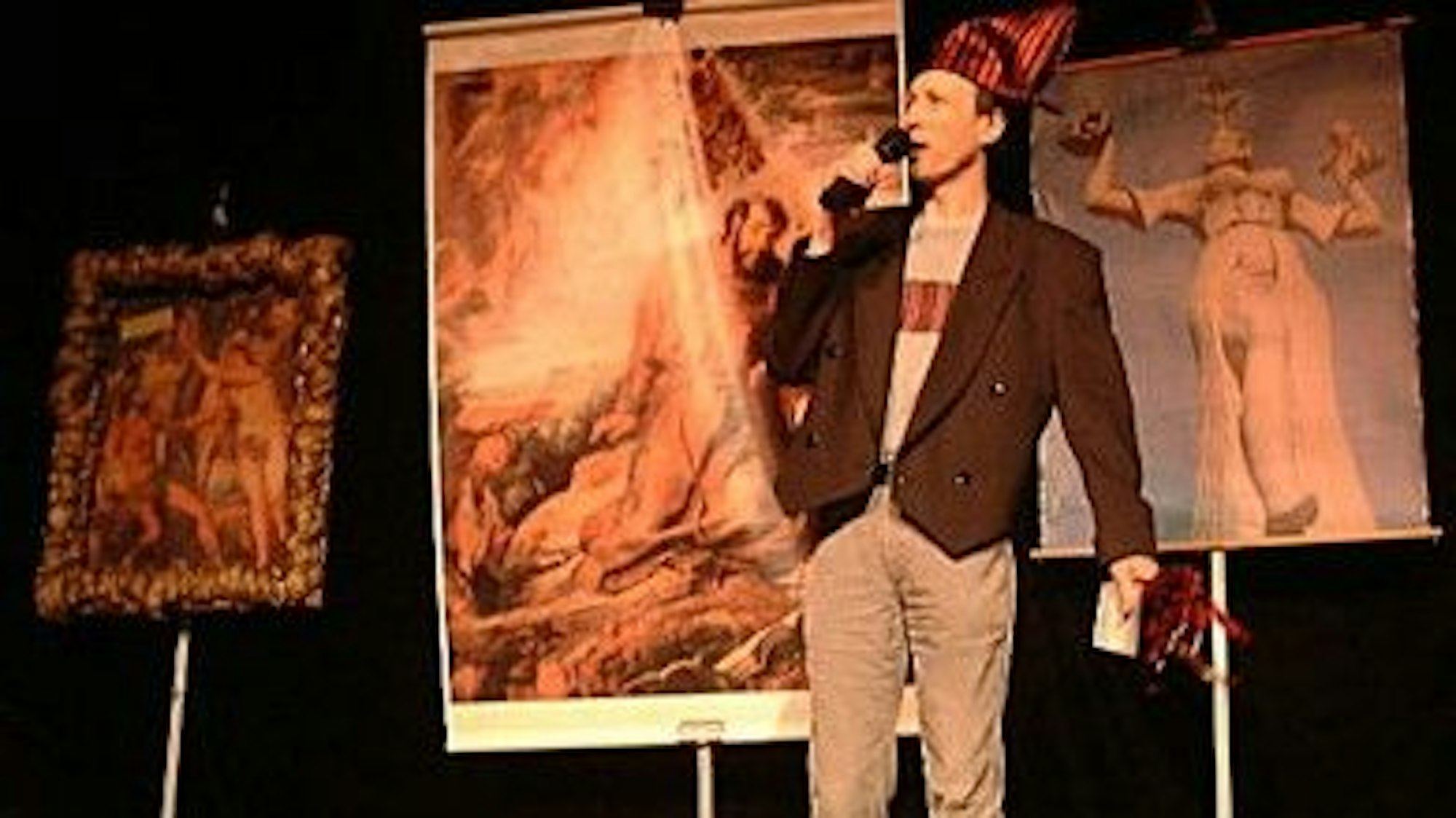 Ein Mann steht vor drei großformatigen Bildern auf einer Bühne.