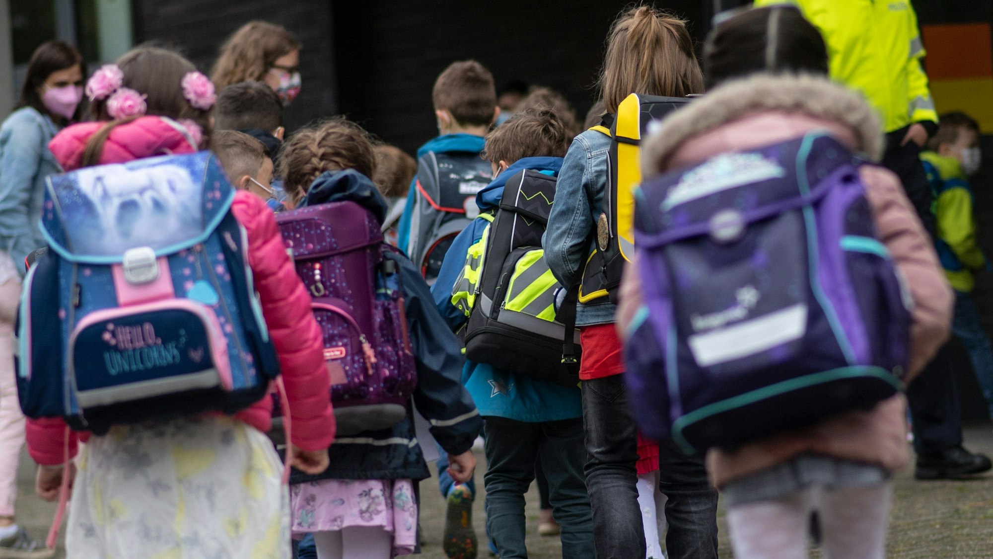 ARCHIV - 18.08.2021, Nordrhein-Westfalen, Wuppertal: Erstklässler mit ihren Schultaschen warten bei der Einschulung auf den gemeinsamen Gang in ihr Klassenzimmer. Die Grundschulklassen sind in Nordrhein-Westfalen so groß wie in keinem anderen Bundesland. Der Landtag debattiert am Donnerstag über die Konsequenzen. (Zu dpa: «Landtag debattiert über volle Klassenzimmer in Grundschulen») Foto: Bernd Thissen/dpa +++ dpa-Bildfunk +++