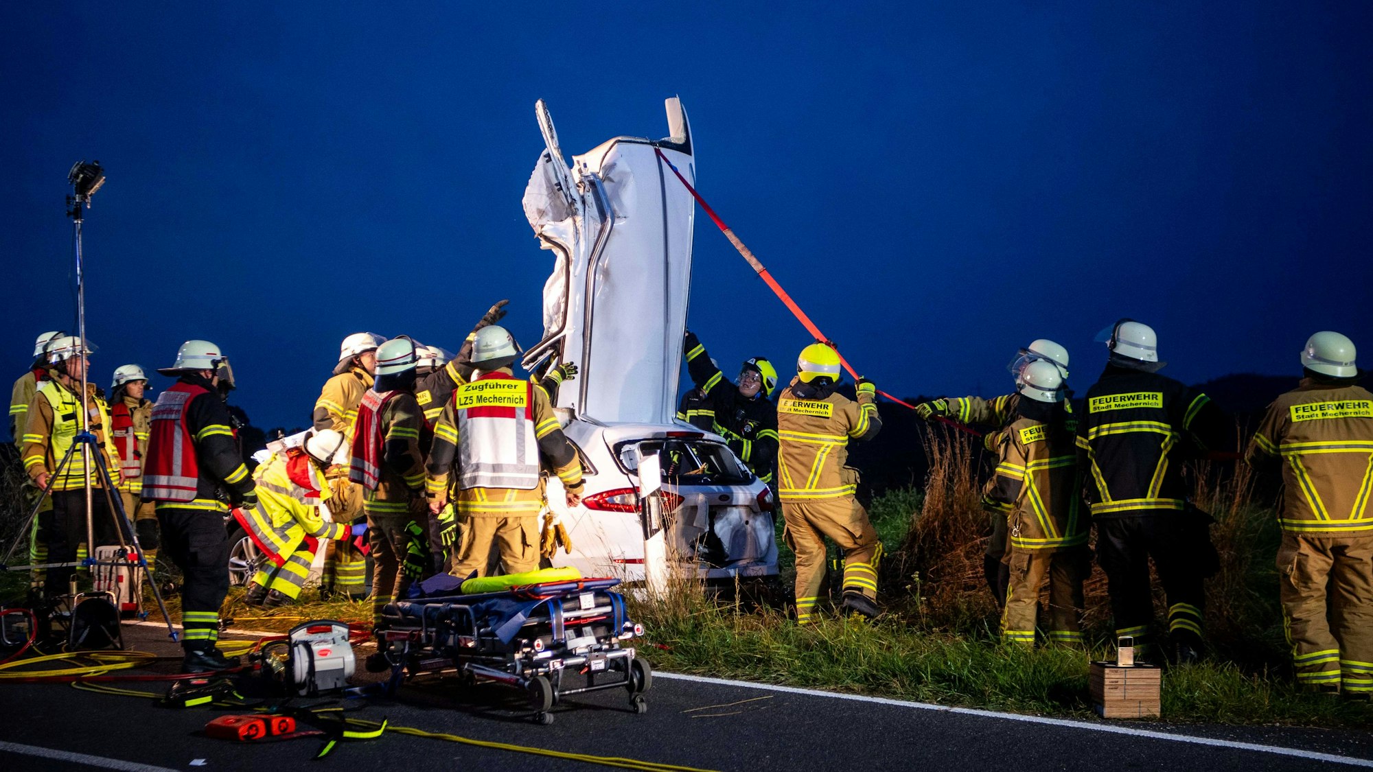 Das Bild zeigt, wie zahlreiche Feuerwehrleute gerade das Dach eines Fahrzeugs abtrennen und nach hinten ziehen.