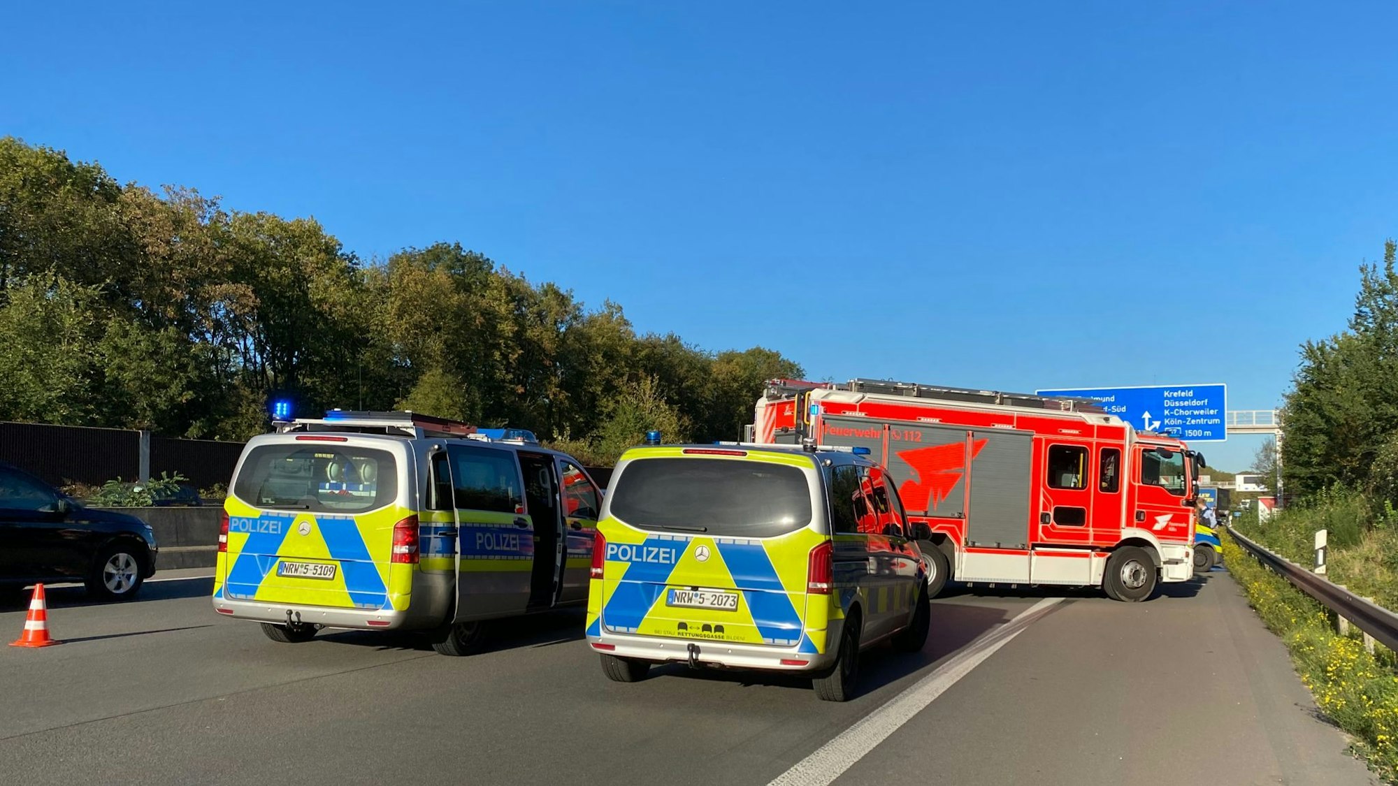 Zwei Polizeiwagen und ein Feuerwehrauto stehen auf einer Autobahn.