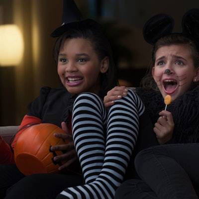 Drei verkleidete Mädchen sitzen schreiend vor dem Fernseher.