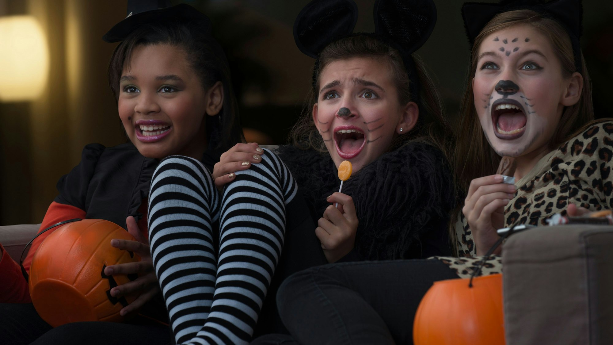 Drei verkleidete Mädchen sitzen schreiend vor dem Fernseher.