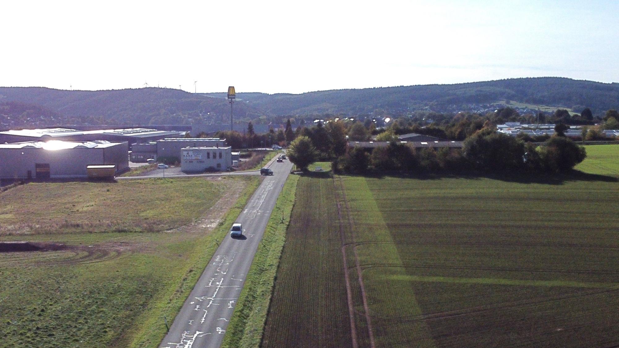 Zu sehen sind auf der Luftaufnahme der von Bäumen verdeckte Heidehof und die Freifläche daneben. Das Gelände wird von einer Straße begrenzt.