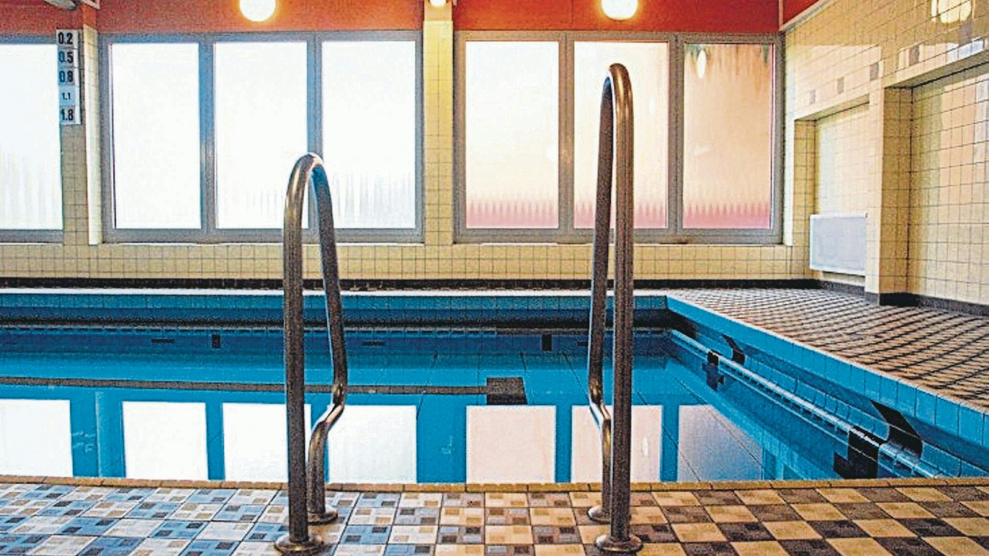 Ein Schwimmbecken mit Einstiegsleiter in einer Schwimmhalle.