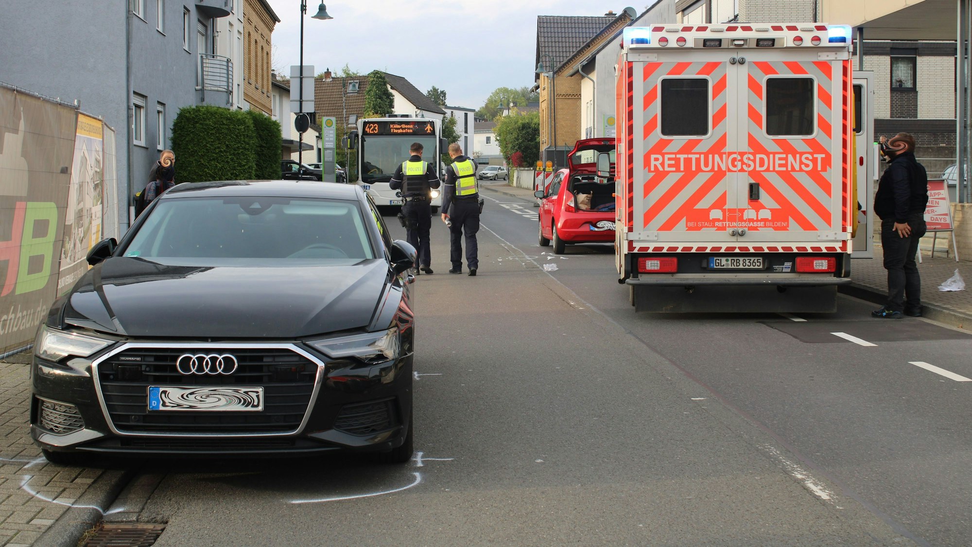 Zwei Unfallautos stehen am Straßenrand, ein Rettungswagen und Polizisten stehen auf der Straße, im Hintergrund wartet ein Linienbus vor der Unfallstelle.