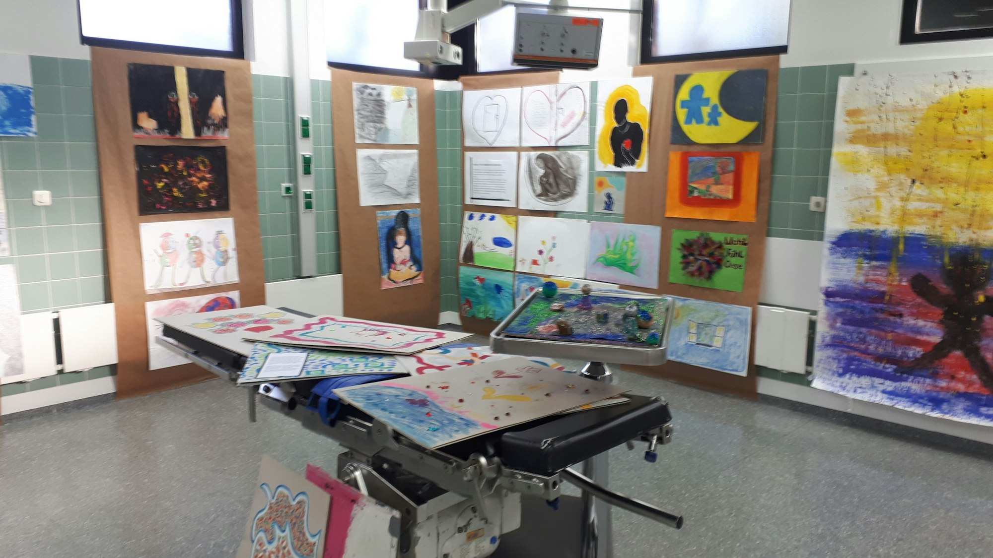 In einem OP-Raum sind einige Arbeiten aus der Kunsttherapie ausgestellt. Die Operationsliege ist aus dem alten Inventar der Räumlichkeiten erhalten geblieben.