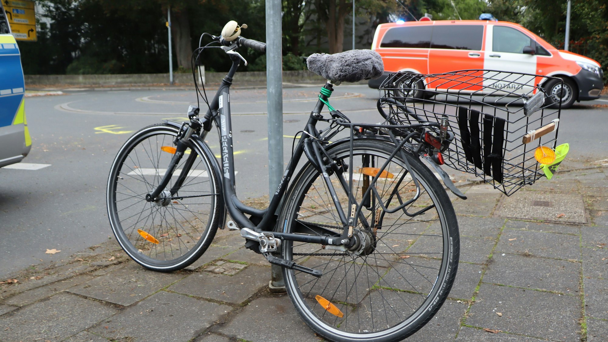 Ein dunkles Fahrrad steht gelehnt an einen Schildpfosten am Kreisverkehr der Brühler Kaiserstraße. Das Rad ist durch den Unfall verbogen.