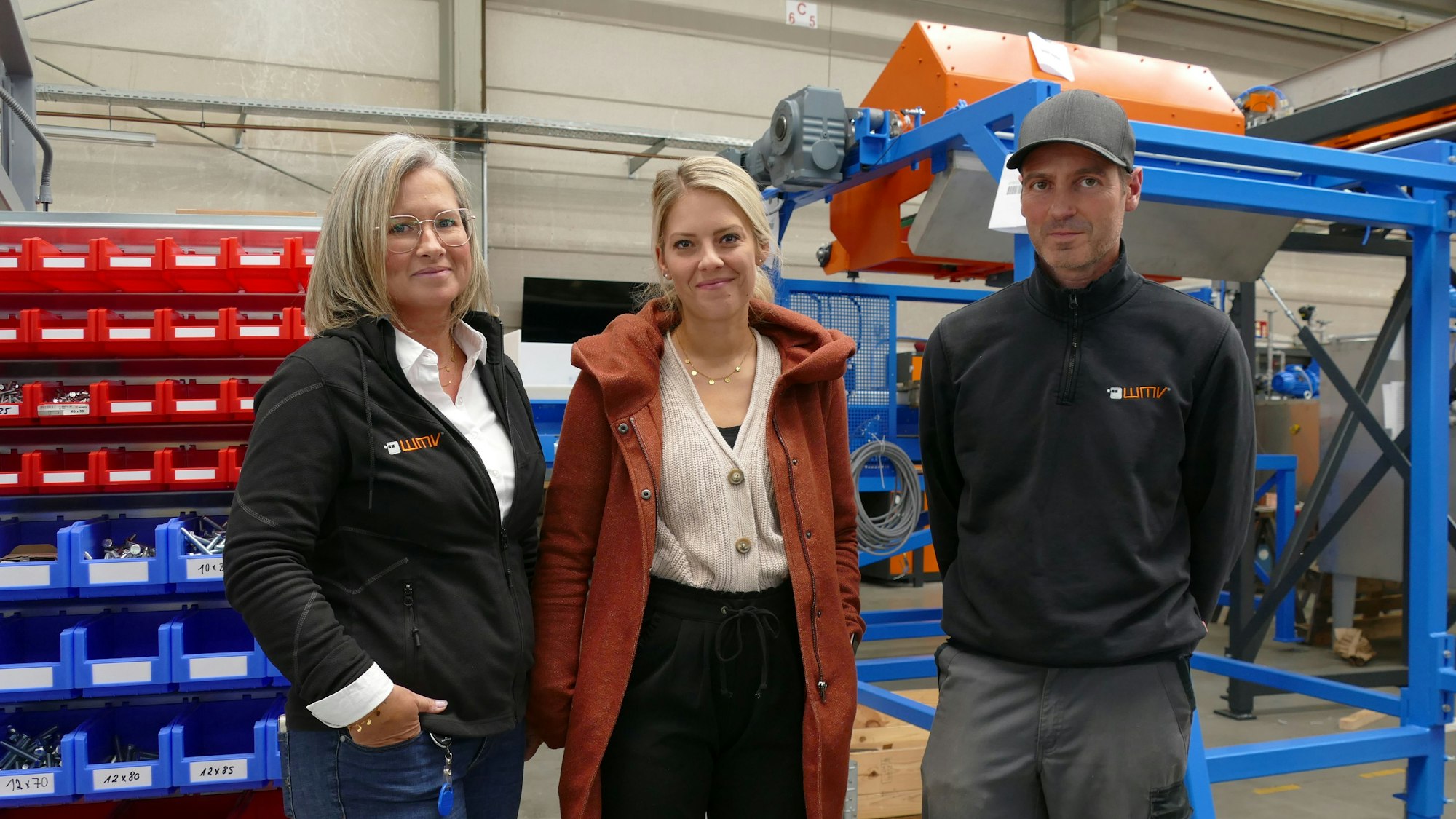 Zwei Frauen und ein Mann blicken in eine Kamera.